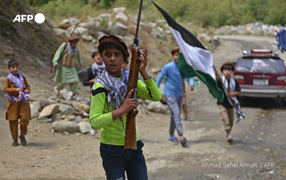 Afghan children carry rifles and a Panjshir National Resistance Front flag along a road in the Dara district of Panjshir province